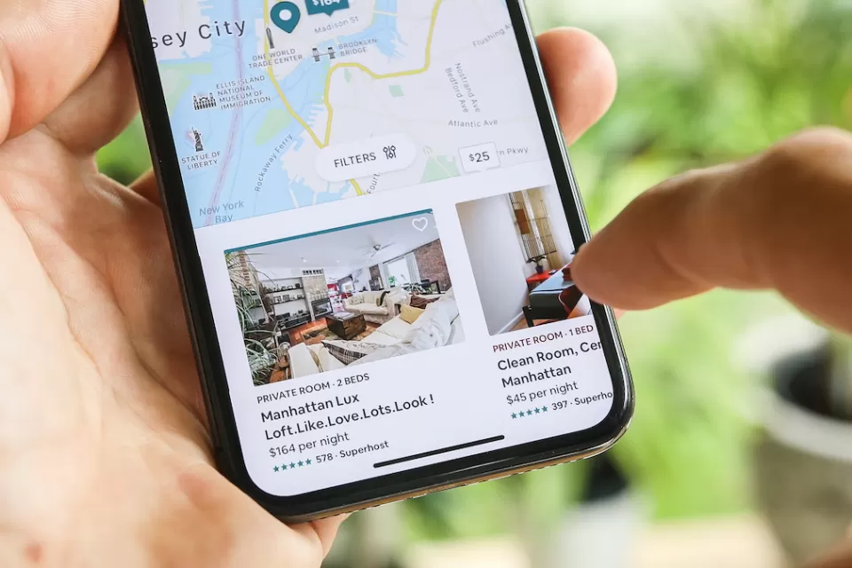 Close-up of hand holding phone with AIrbnb app open to New York City listings